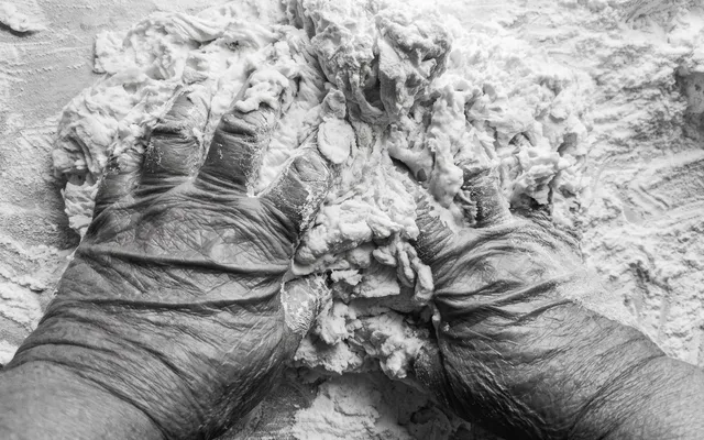 Mani segnate dal lavoro che impastano la farina, in bianco e nero