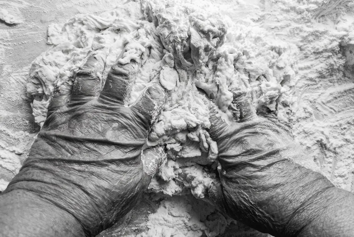 Mani segnate dal lavoro che impastano la farina, in bianco e nero