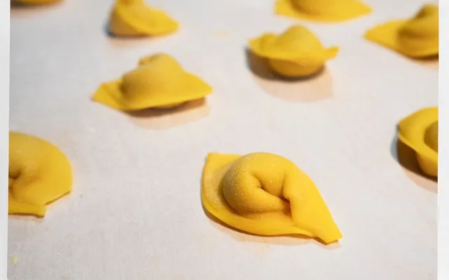 Cappelletti crudi appena chiusi, con la punta alzata, sul piano infarinato