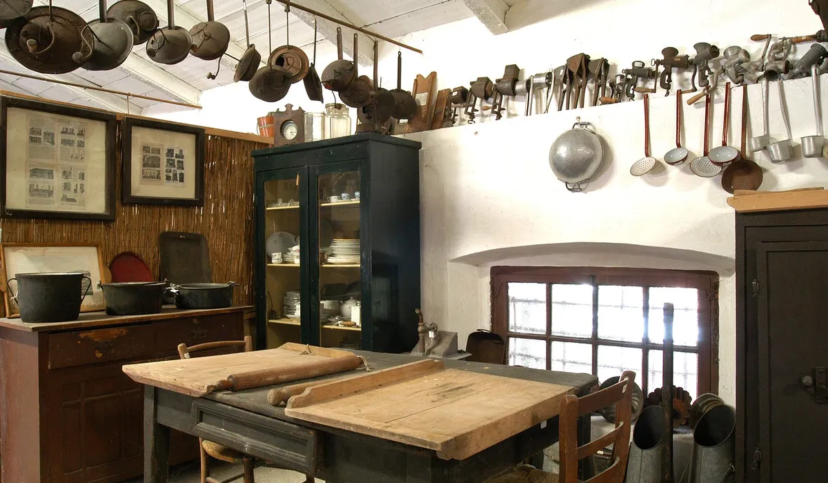 Cucina contadina tradizionale con il grande tavolo di lavoro in legno al centro e i rami appesi alla parete