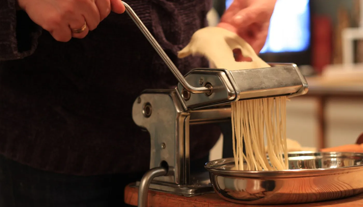 Mani alla manovella della macchina per la pasta mentre i tagliolini escono dal rullo