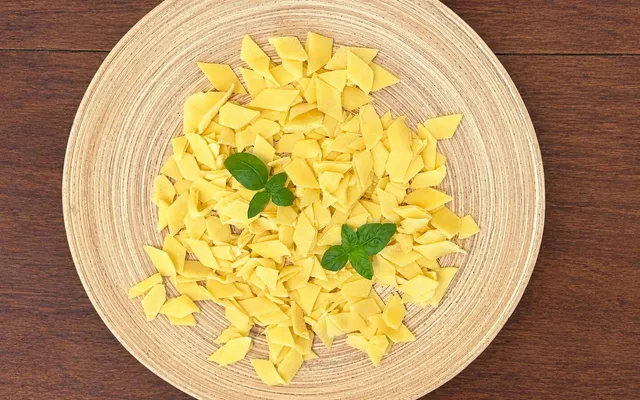 Maltagliati crudi dai bordi irregolari nel piatto di paglia, con due foglie di basilico