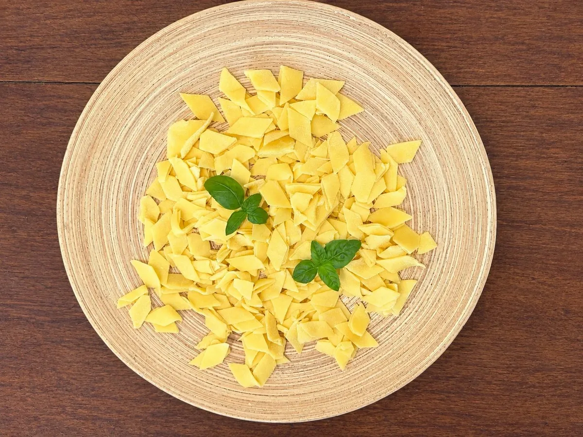 Raw maltagliati with their irregular edges on a straw plate, with two basil leaves