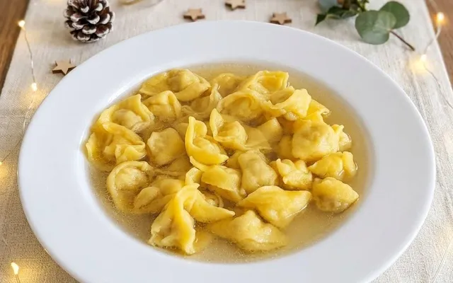 Piatto fondo di cappelletti nel brodo su una tavola di Natale, tra lucine, pigna e rametti di eucalipto