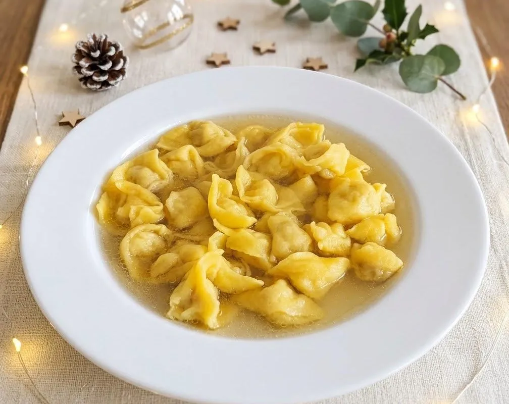 Piatto fondo di cappelletti nel brodo su una tavola di Natale, tra lucine, pigna e rametti di eucalipto