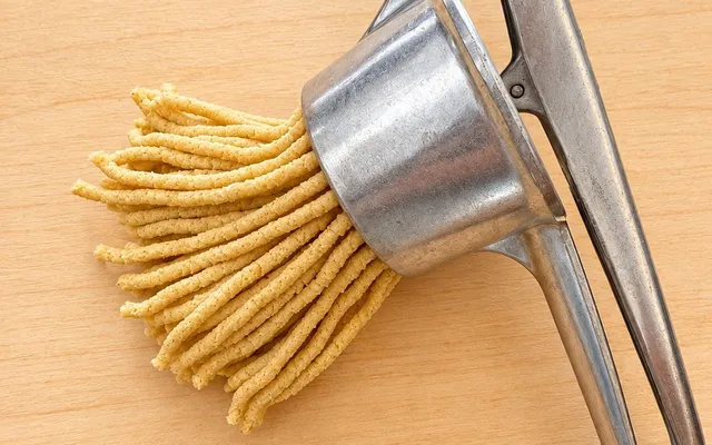 Passatelli appena usciti dallo schiacciapatate, con il ferro appoggiato sul tagliere