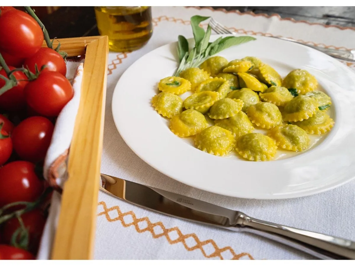 Ravioli di ricotta e spinaci nel piatto con burro e salvia, accanto ai pomodori