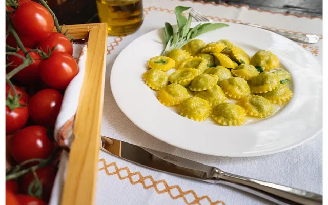 Ravioli di ricotta e spinaci nel piatto con burro e salvia, accanto ai pomodori
