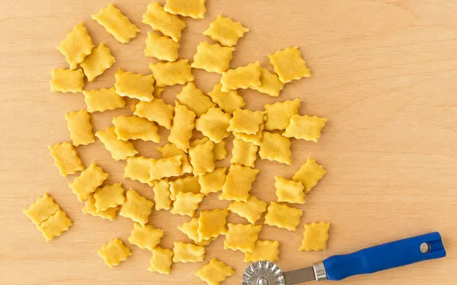 Quadratini di spoja lorda con il bordo smerlato sparsi sul tagliere, accanto alla rotella dentata