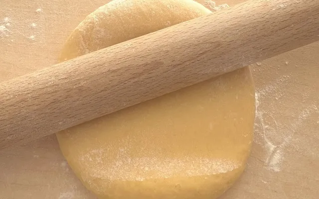 Il mattarello lungo appoggiato sul disco di impasto giallo, sul tagliere infarinato
