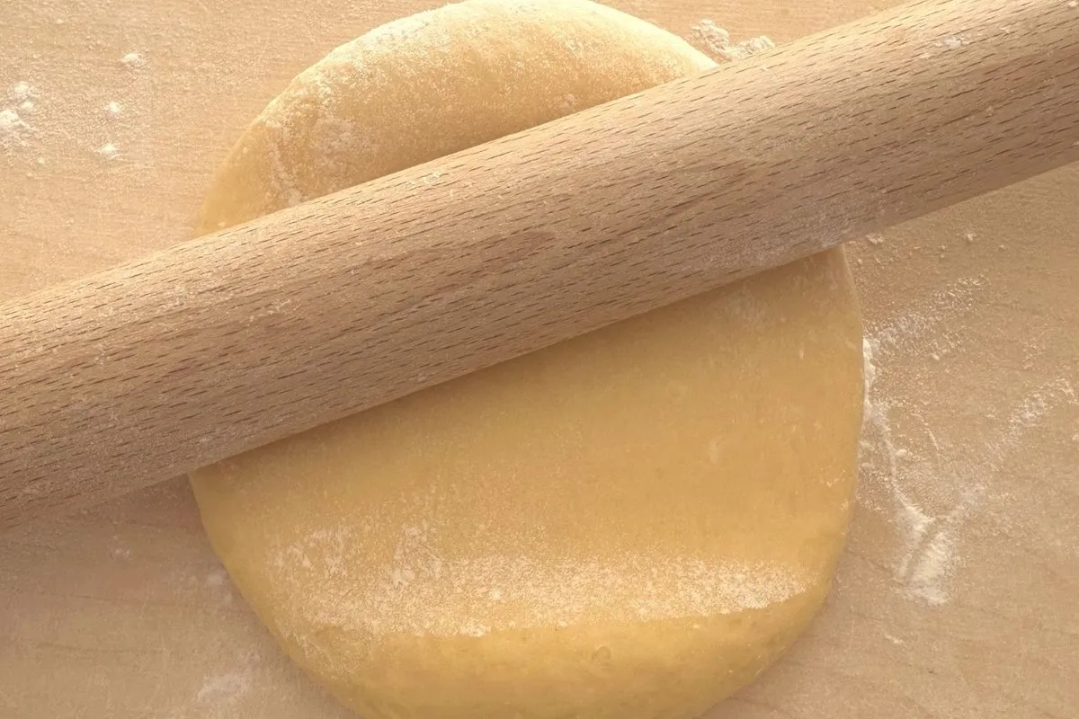 Il mattarello lungo appoggiato sul disco di impasto giallo, sul tagliere infarinato