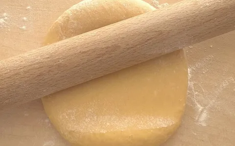 Il mattarello lungo appoggiato sul disco di impasto giallo, sul tagliere infarinato