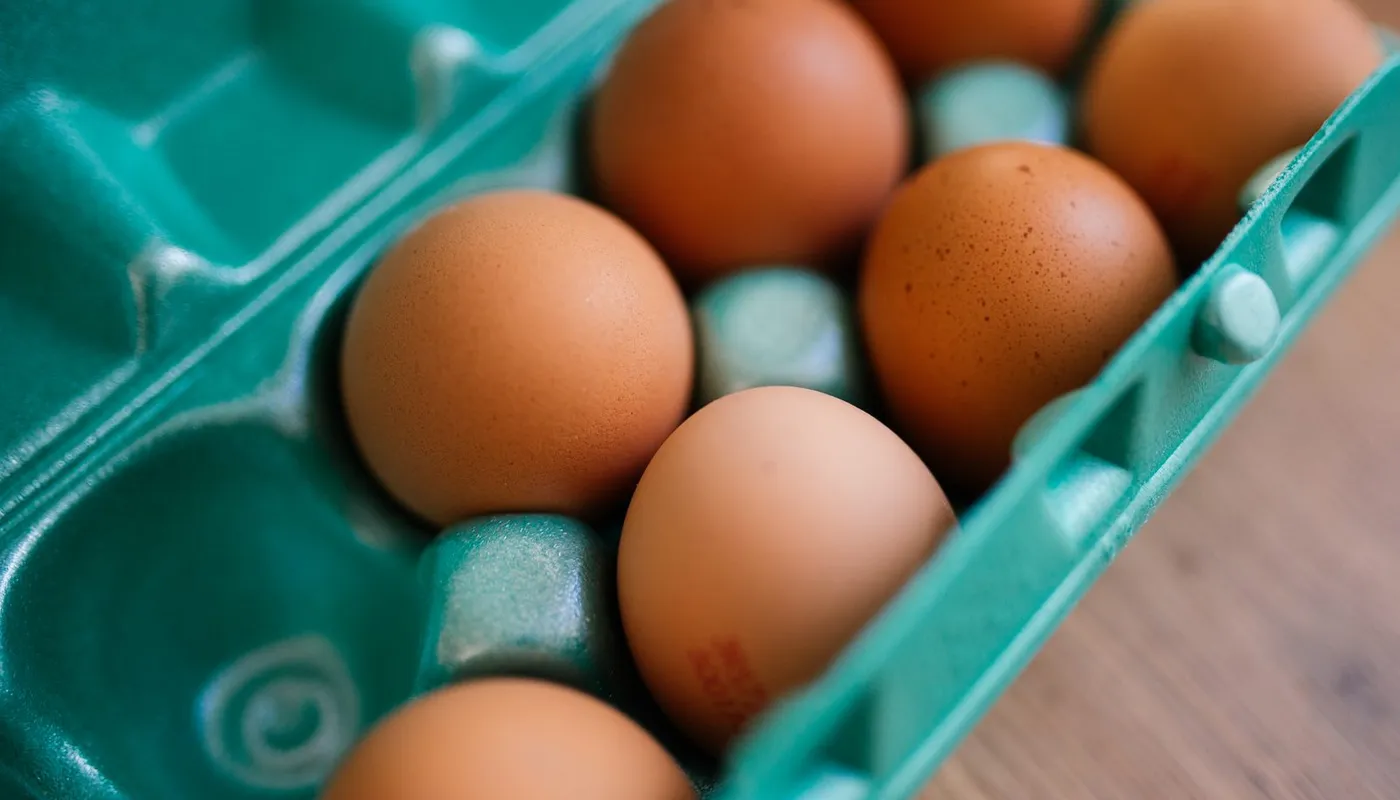 Uova fresche dal guscio scuro in un cartone, sul piano di legno della cucina