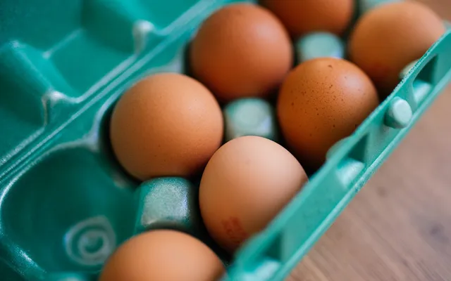 Uova fresche dal guscio scuro in un cartone, sul piano di legno della cucina